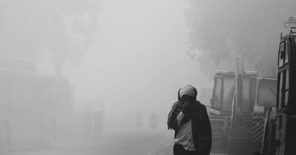 A person walks through a foggy street in Delhi, capturing the city's atmospheric haze.